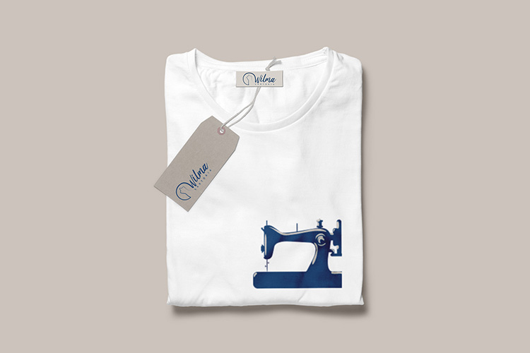 Realizzazione grafica Etichetta vestiti Wilma Sartoria testo blu navy su cartoncino naturale colore beige e design t-shirt bianca rappresentante una macchina da cucire blu