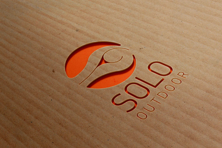Realizzazione grafica Logo Solo con pittogramma ad occhio, il naming Solo con font bold e il pay-off Outdoor intagliato su cartone alveolare naturale e la parte bucata mostra l'arancione sottostante